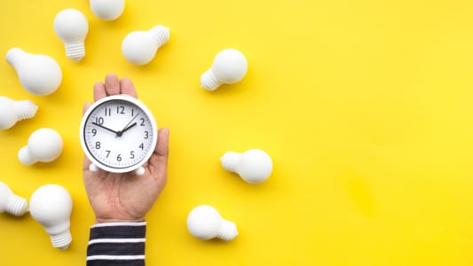 Quelqu'un tient une horloge sur fond jaune avec des ampoules tout autour.
