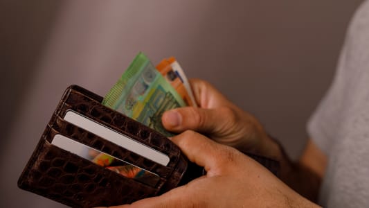Gros plan des mains d'une personne tenant un portefeuille en cuir marron rempli de billets en euros et de cartes de crédit