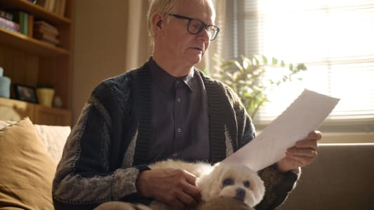 Un homme &acirc;g&eacute; lit un document tout en &eacute;tant assis avec son chien de compagnie.