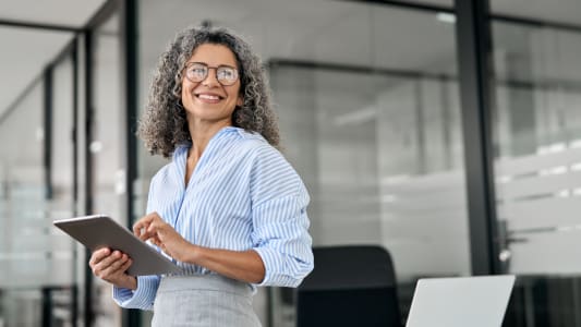 Femme d'affaires professionnelle mature souriante, directrice de banque plus &acirc;g&eacute;e, femme ex&eacute;cutive heureuse ou entrepreneuse &acirc;g&eacute;e tenant une tablette num&eacute;rique debout dans le bureau au travail, regardant ailleurs dans l'espace de copie.