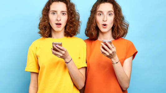 Jumeaux &eacute;motionnels surpris avec la bouche grande ouverte et les yeux &eacute;carquill&eacute;s tenant des smartphones et regardant la cam&eacute;ra. Vente, commerce, message gratuit, doubles r&eacute;ductions
