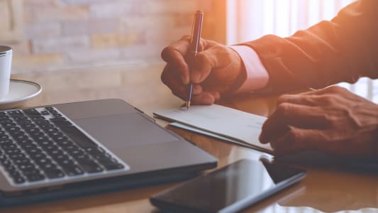 Un homme d'affaires écrit et signe un chèque avec un ordinateur portable sur la table en bois d'un bureau moderne à domicile.