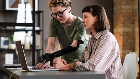 Une jeune femme avec une prothèse au bras pointant un ordinateur portable.