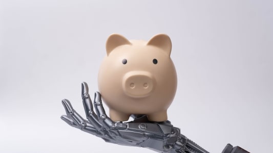 Main robotique futuriste tenant une tirelire, symbolisant l'intelligence artificielle dans la finance, les économies intelligentes, la banque numérique, la technologie d'investissement et les solutions de gestion d'argent automatisées.