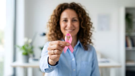 Femme souriante tenant un ruban rose de sensibilisation.