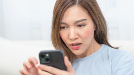 Gros plan d'une jeune femme asiatique regardant son smartphone avec une expression choqu&eacute;e et inqui&egrave;te. Concept d'escroqueries en ligne, de fraude num&eacute;rique, de hame&ccedil;onnage et de cybers&eacute;curit&eacute;.