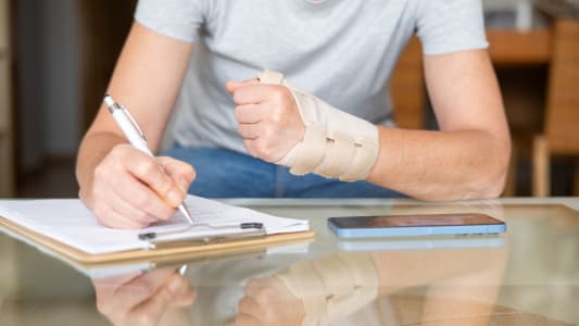 Une femme portant une attelle orthopédique au poignet remplit des documents.