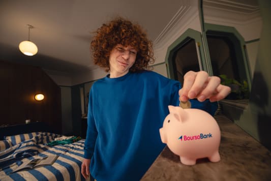 Jeune homme met une pièce dans une tirelire Boursobank.