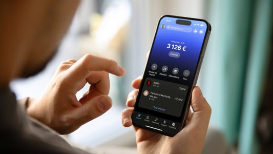Un homme utilise un smartphone à écran vide au design moderne sans cadre tout en étant assis sur une chaise à l'intérieur de la maison