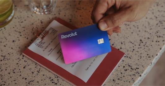 Carte Revolut tenue au-dessus d'une addition sur une table.