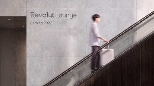 Homme flou sur escalator, valise, panneau Revolut Lounge.