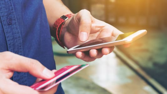 Un homme tient un mobile et une carte bancaire