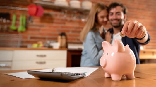 Un couple souriant met de l'argent dans une tirelire