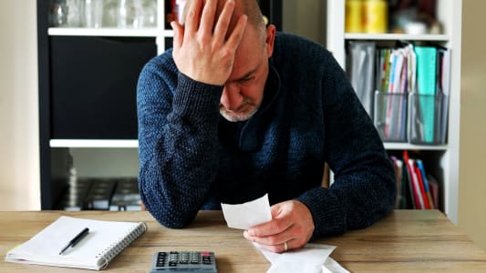 Un homme se prend la tte dans les mains en regardant un document avec une calculatrice  ct. 