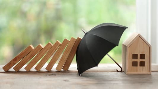 Une maison miniature protge par un parapluie.