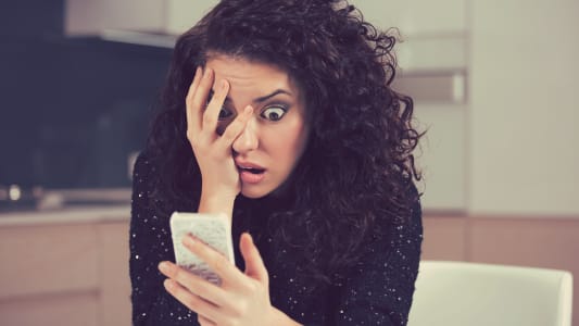 Une femme regarde son tlphone l'air surpris.