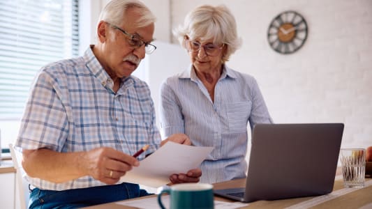 Deux personnes ges regardent un document et un ordinateur.