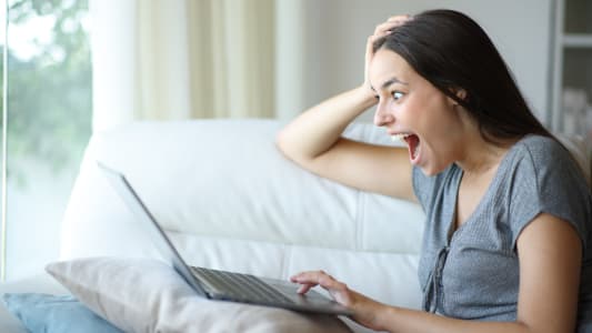 Une femme regarde son ordinateur l'air surpris