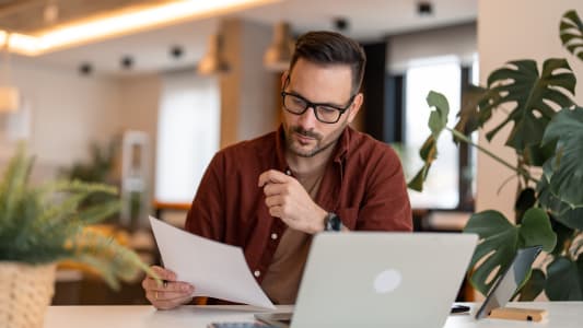 Un homme regarde son ordinateur et des documents.