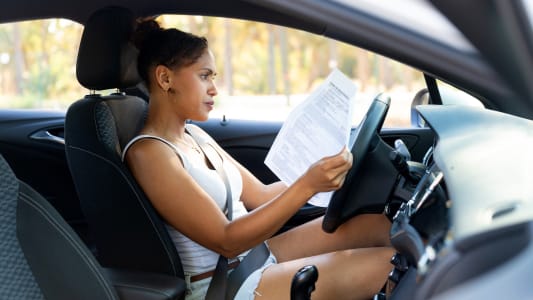 Une femme au volant d'une voiture avec des documents.